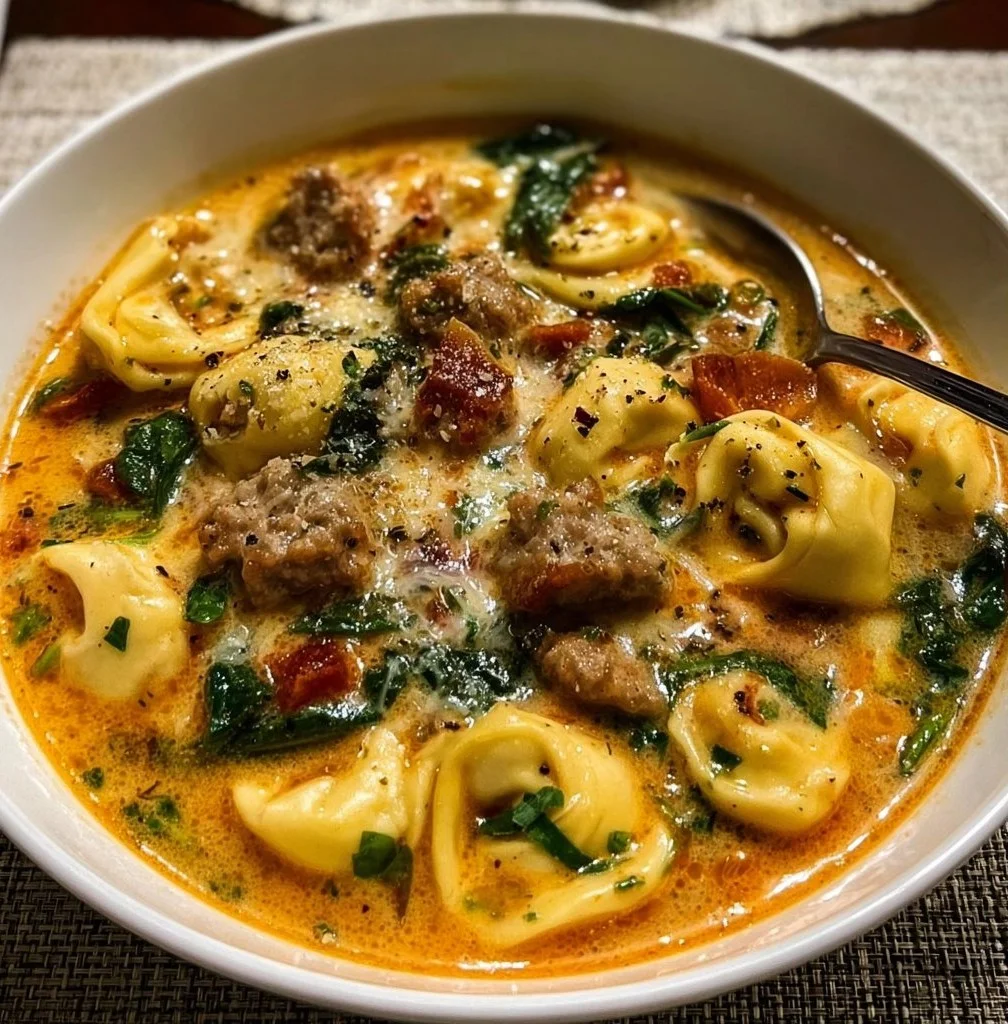Crockpot Sausage and Tortellini Soup simmering in a pot with fresh herbs.